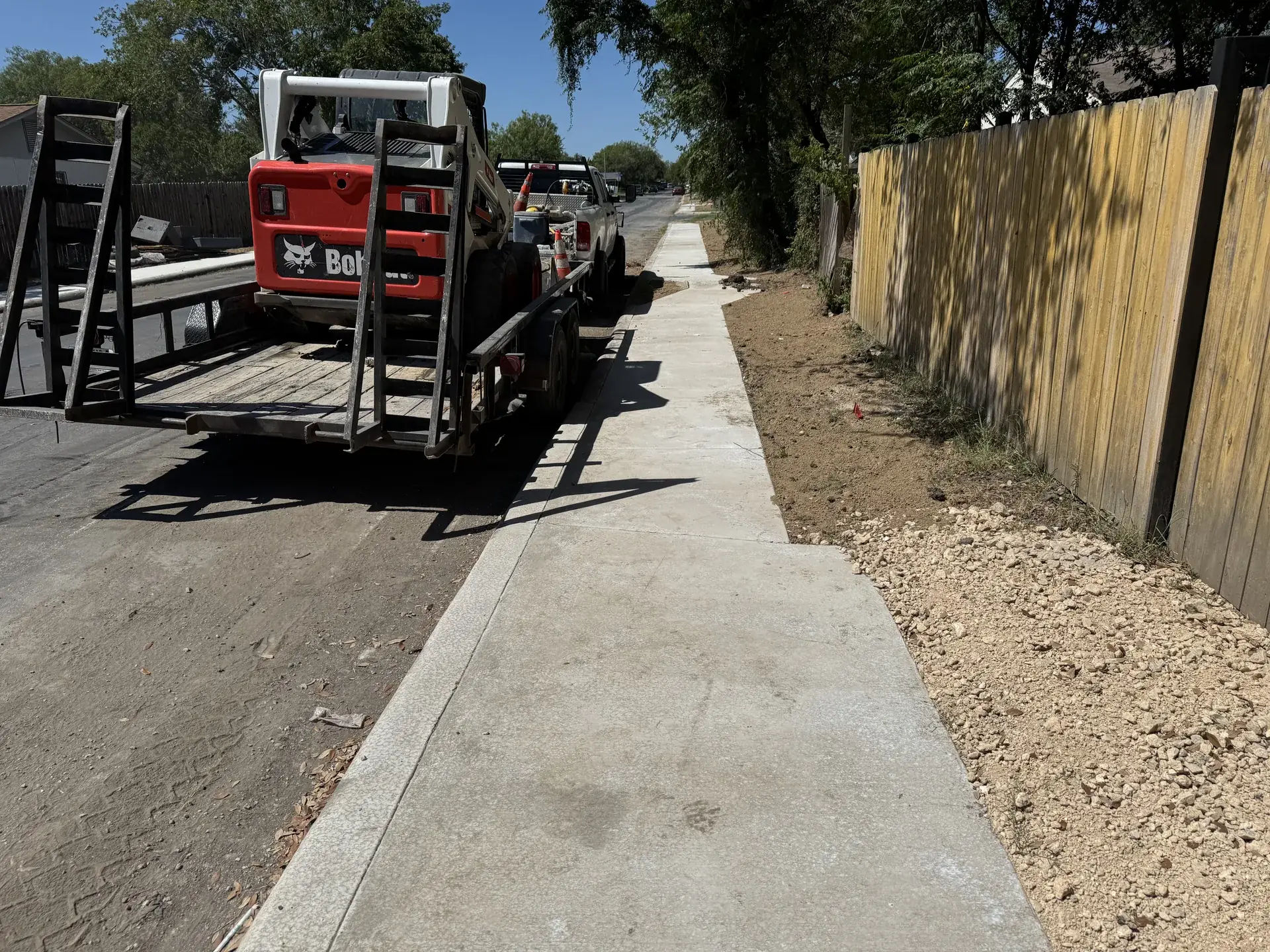 Five Star Trucking skid steer on its trailer beside a new sidewalk in San Antonio, TX