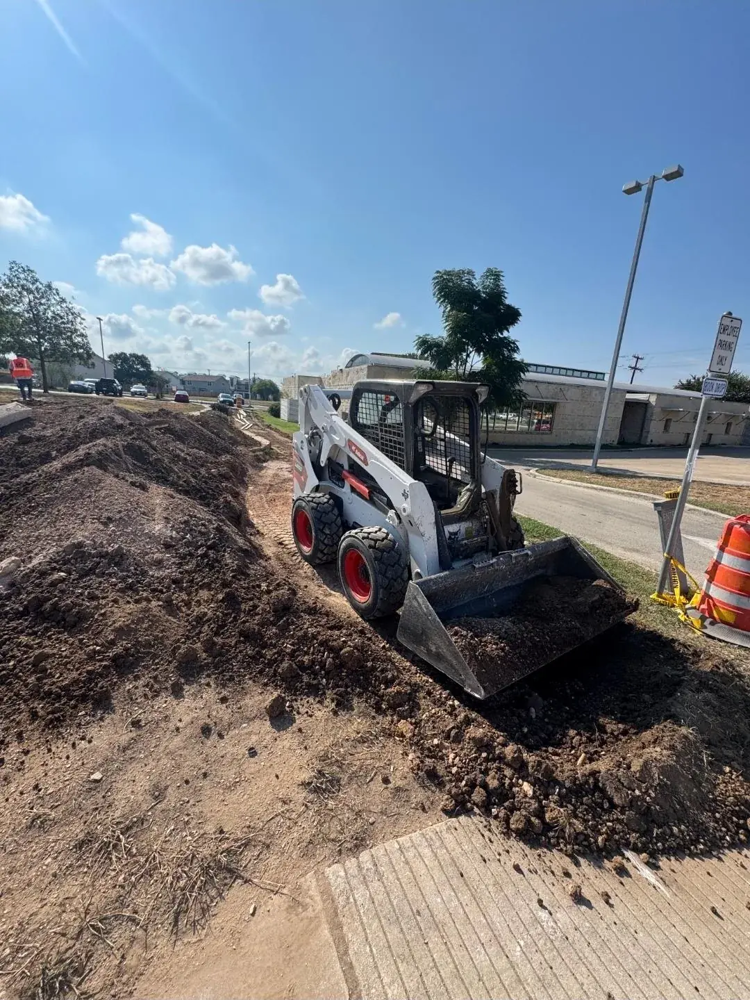 Skid steer spreading delivered topsoil along a roadside
